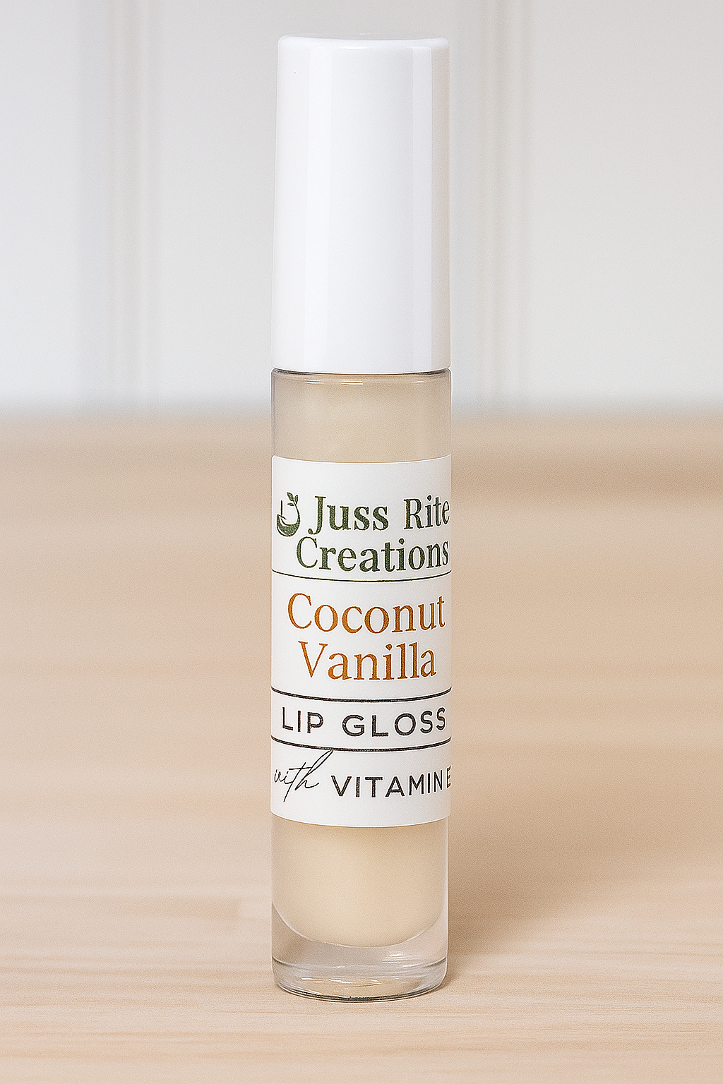 Lip gloss bottle labeled 'Coconut Vanilla' by Juss Rite Creations on a wooden surface.