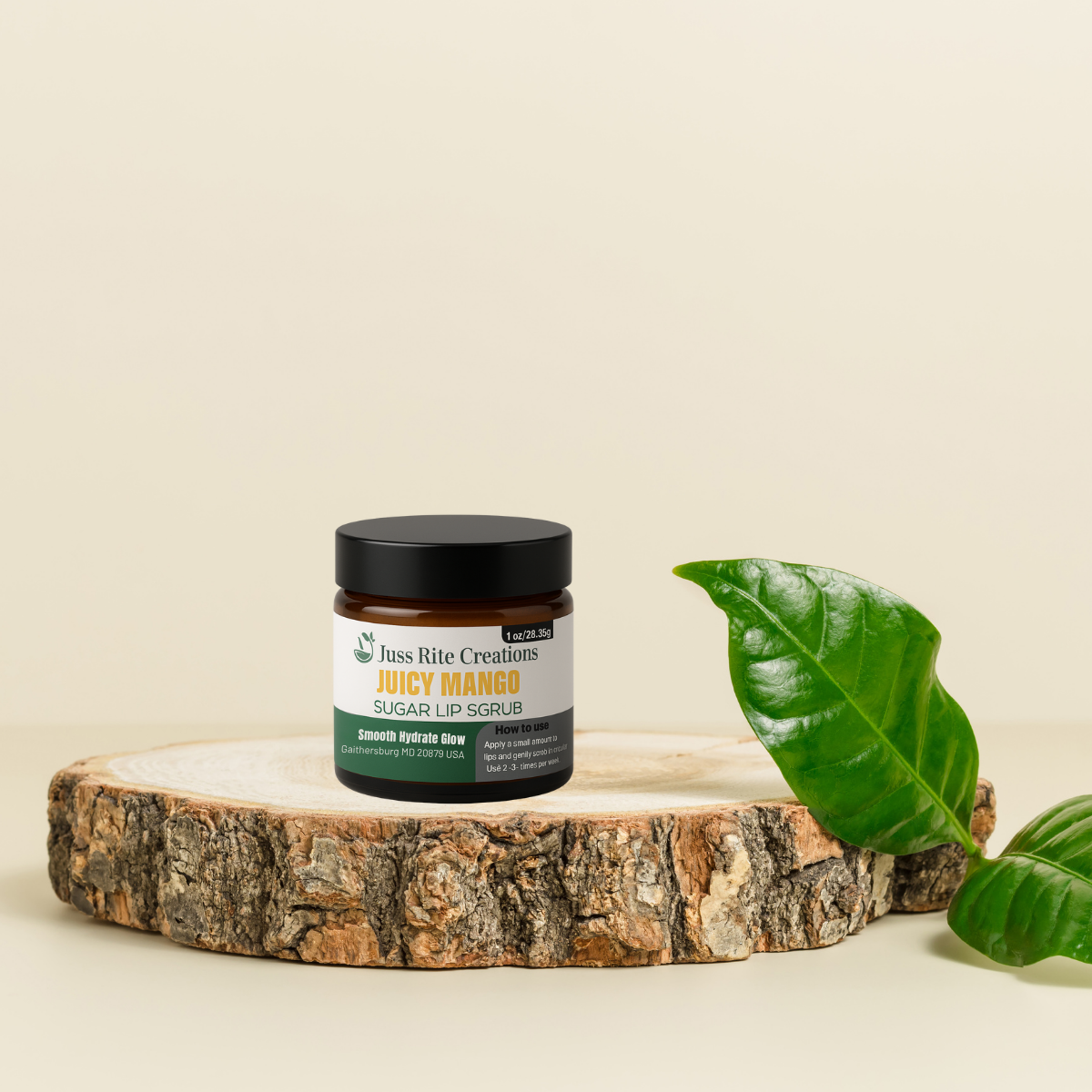 Jar of 'Juicy Mango' sugar lip scrub on a wooden platform with a green leaf on a beige background