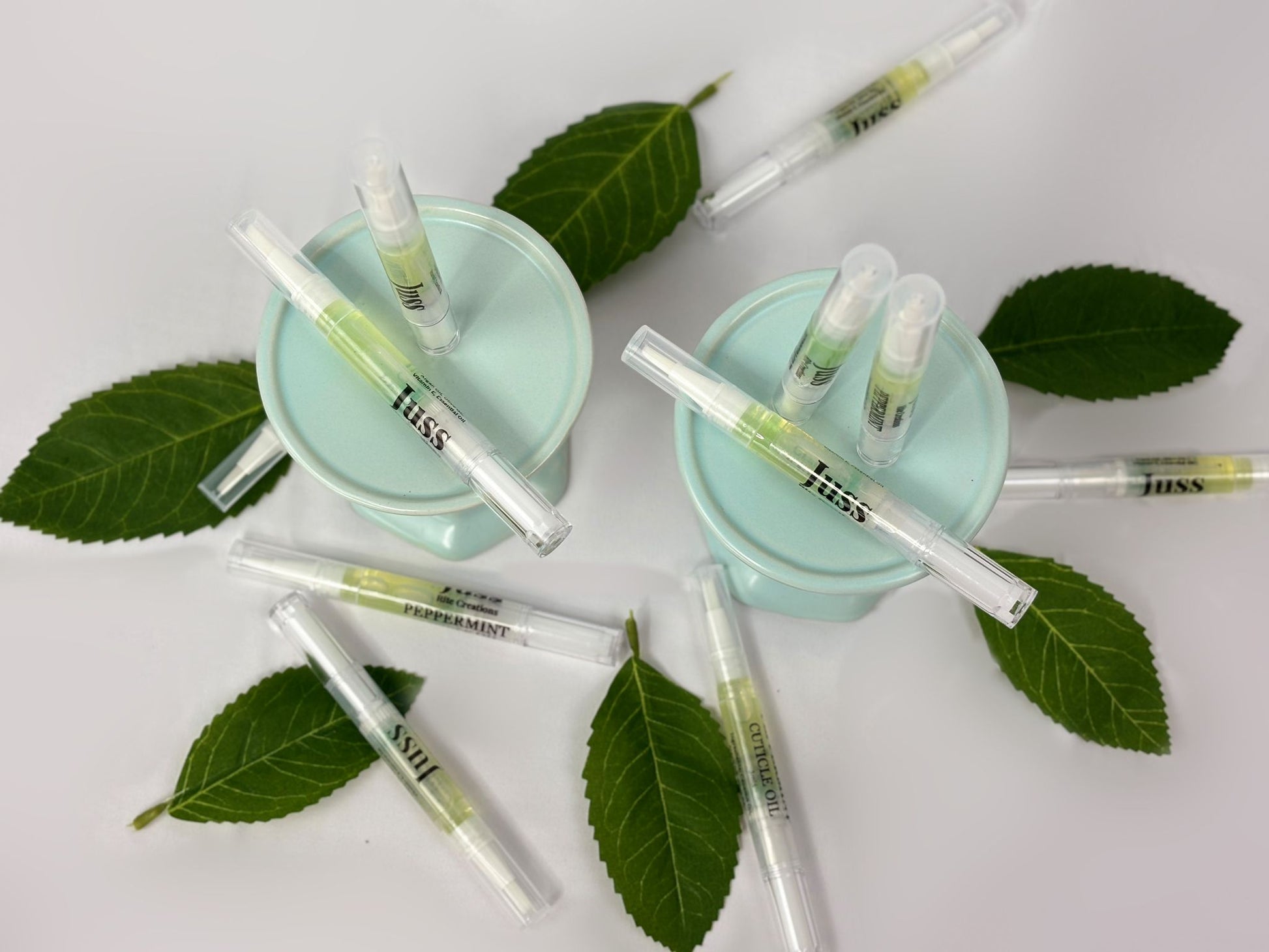 Juss Rite creations cuticle oil pens with green leaves on a white background