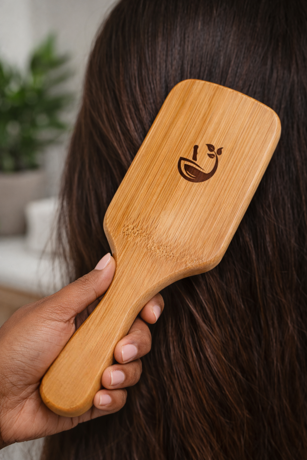 Person using a wooden paddle brush on their hair with a blurred indoor background