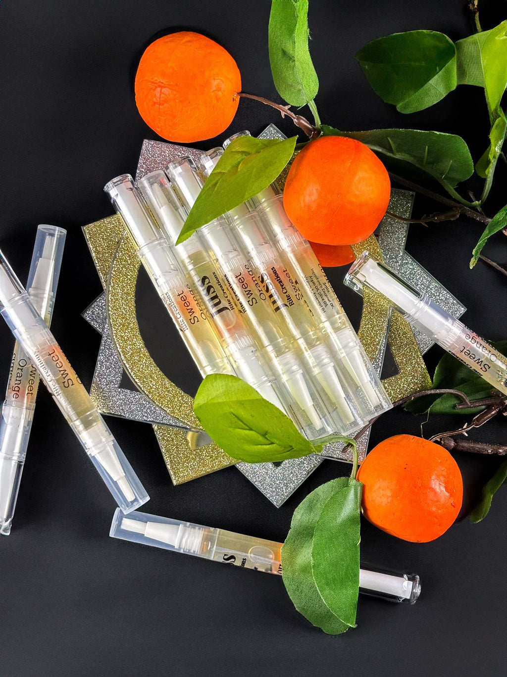 Orange cuticle oil pens and mandarin oranges on a dark background