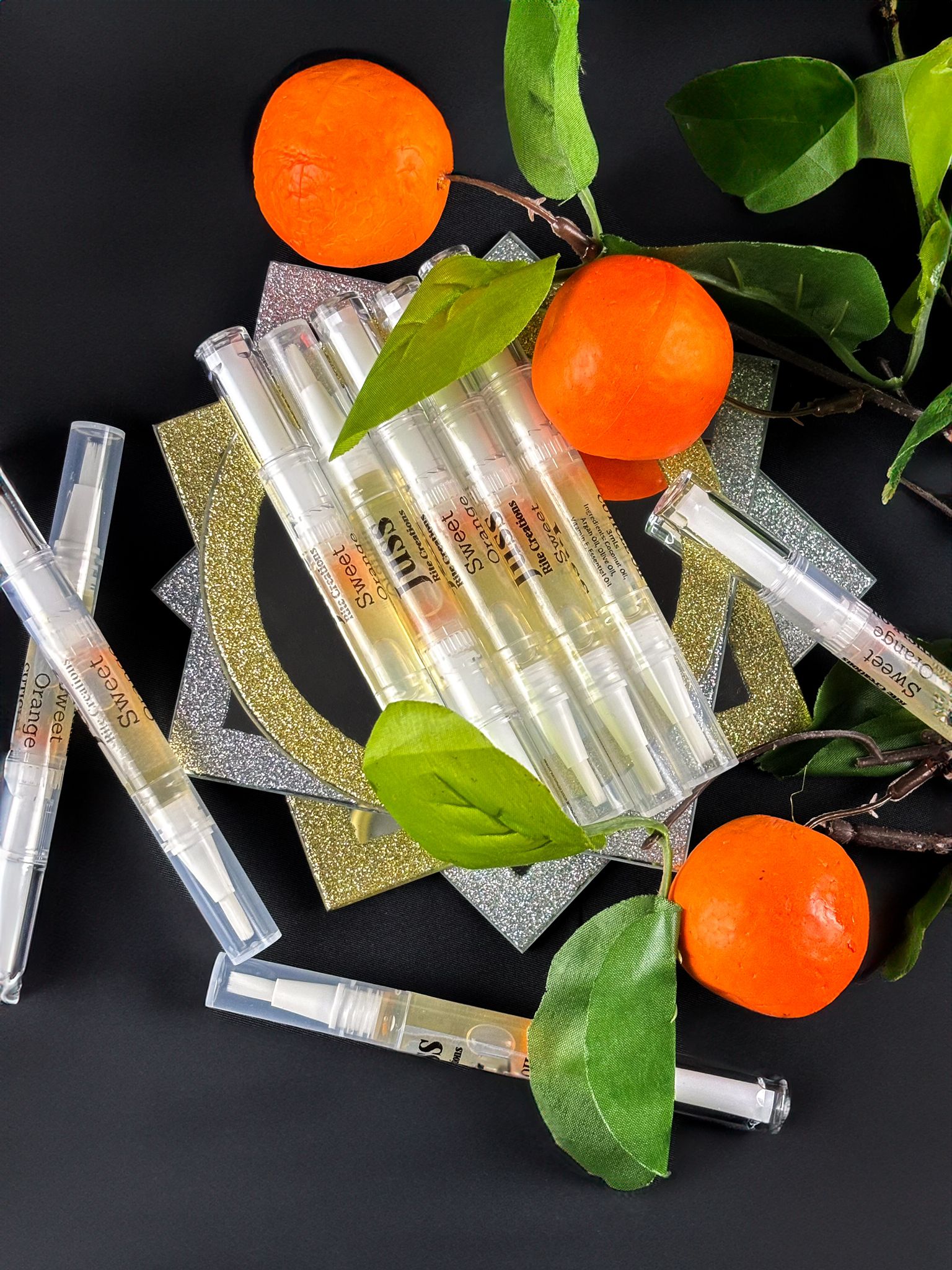 Orange cuticle oil pens and mandarin oranges on a dark background