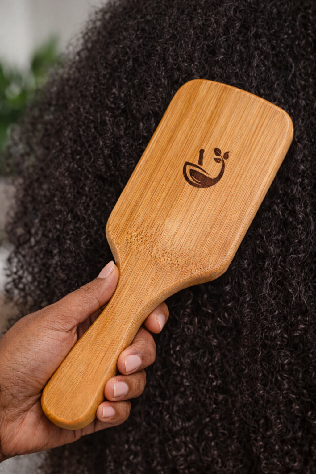 Wooden paddle brush held by a hand with a person's hair in the background
