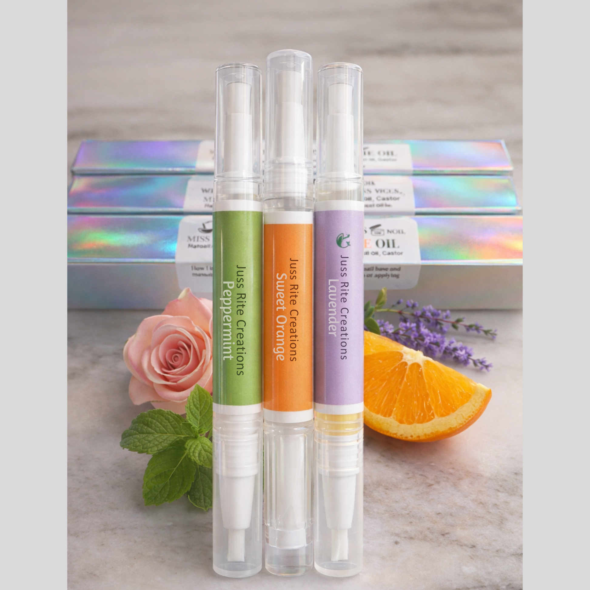 Three small spray bottles with colorful labels on a marble surface with flowers and an orange.