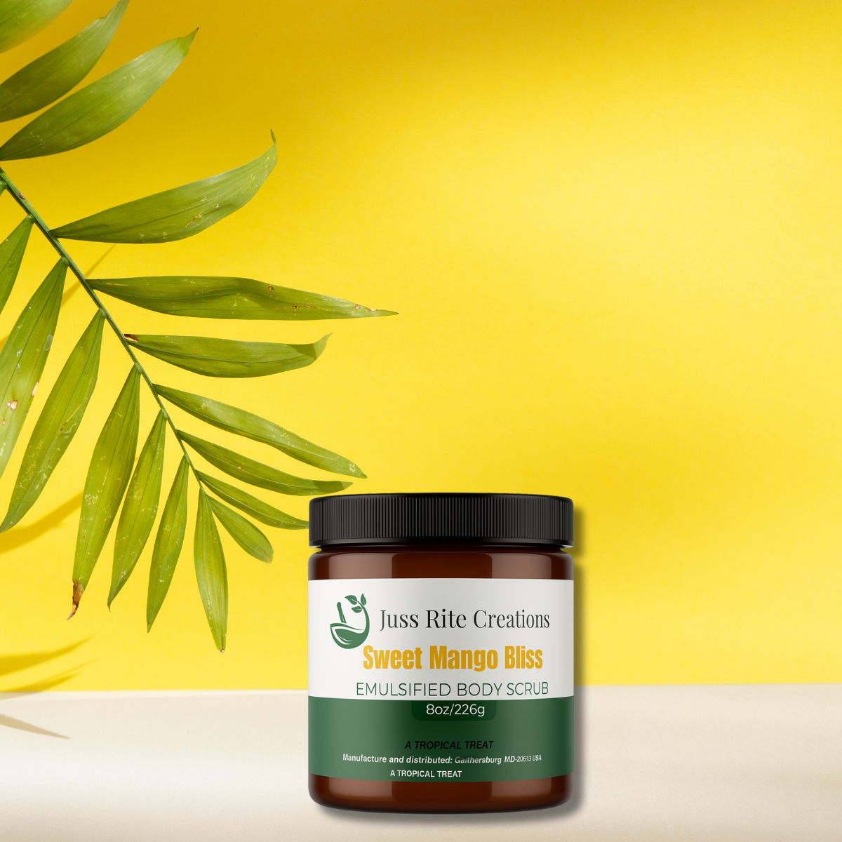 Jar of 'Sweet Mango Bliss' emulsified body scrub with a palm leaf on a yellow background