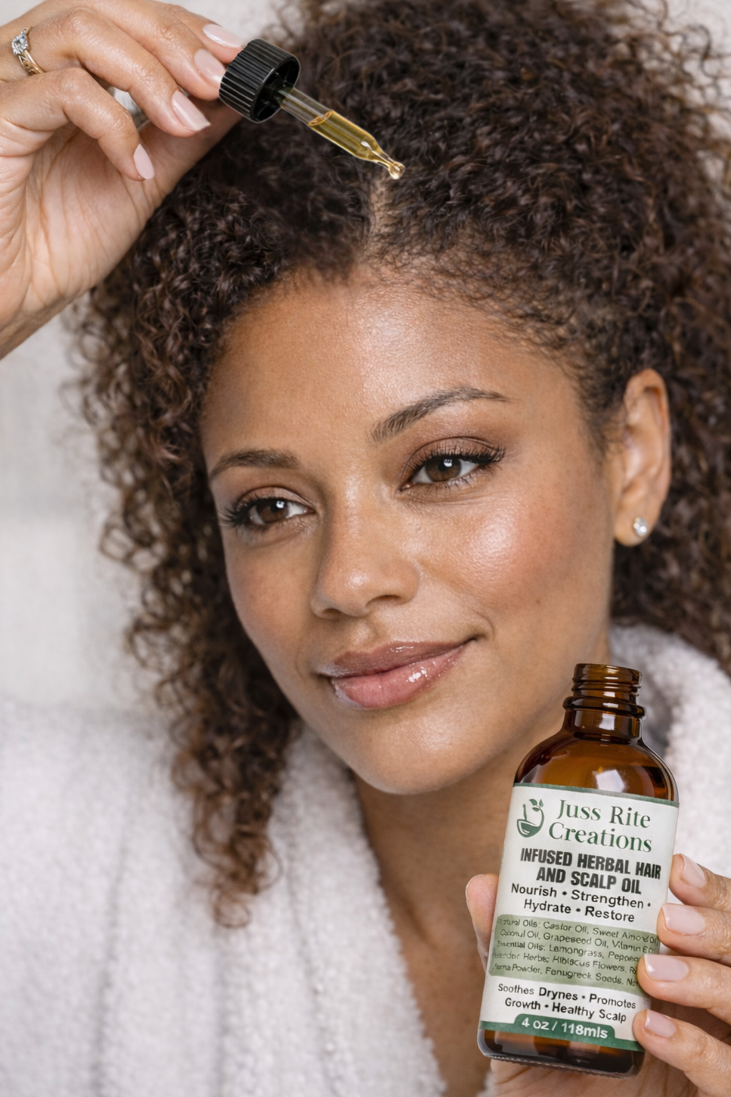 Woman applying hair oil to her hair with a dropper bottle, holding a bottle of Juss Rite Creations product.